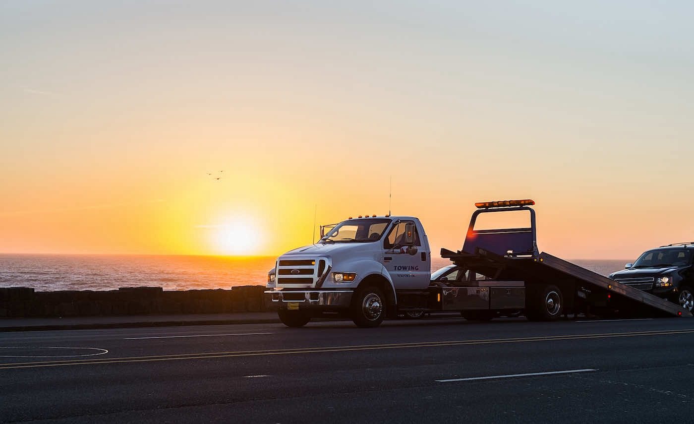 Flatbed tow truck on a coastal highway at sunset