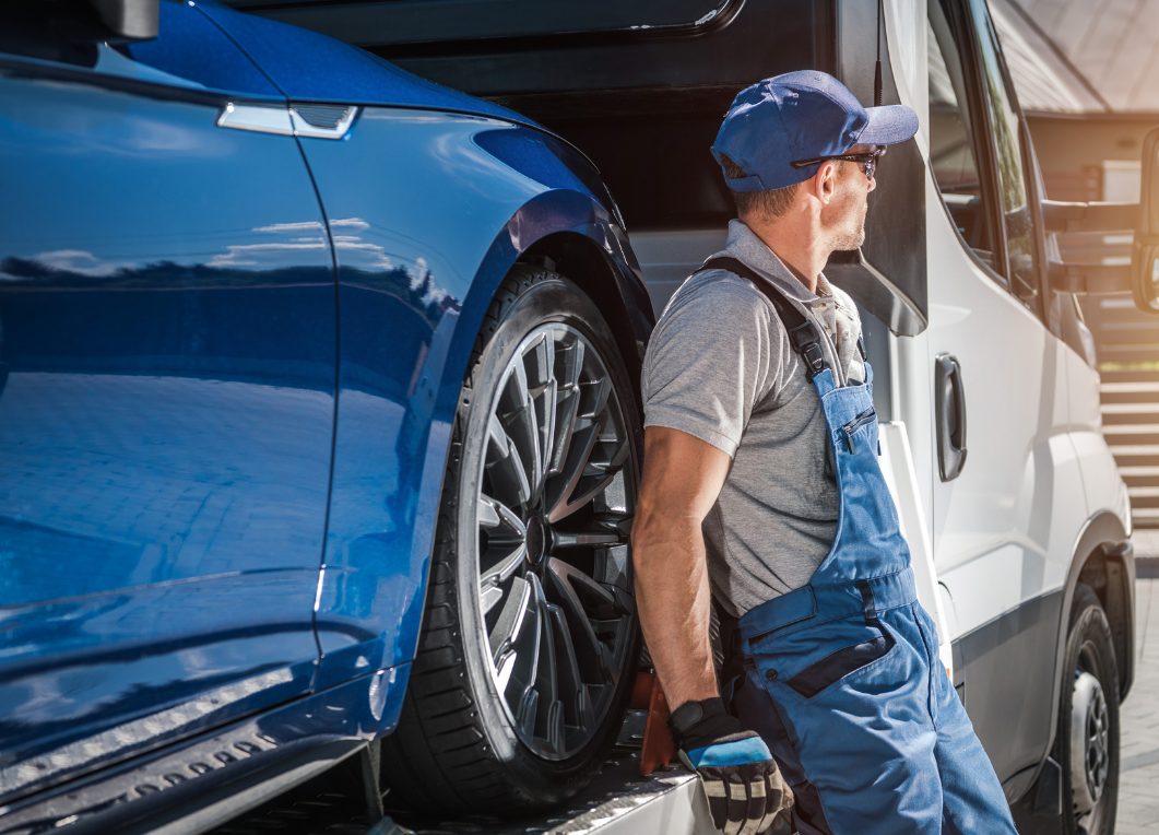 Tow truck operator carrying straps beside a loaded car